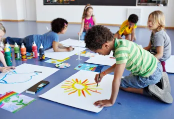 A group of six school age children set up with painting supplies and canvases on the floor painting.
