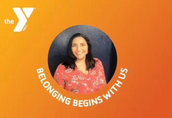 orange gradient background with white Y logo top left. Image of woman centered in circle. Curved white text beneath image reads Belonging Begins With Us