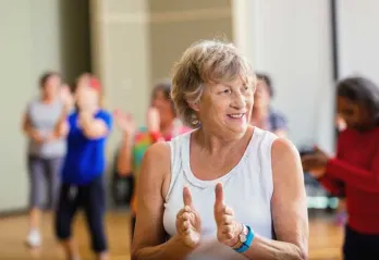 senior woman smiling and clapping in an indoor group exercise class