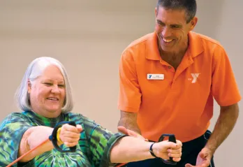 Senior using resistance bands in hands with a trainer.