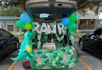 Open car trunk decorated in dinosaur in the jungle theme in a parking lot at a Trunk or Treat event.