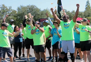 The winning team of the Corporate Cup Challenge, all wearing bright green shirts, cheer when they learned they won the 2022 games.