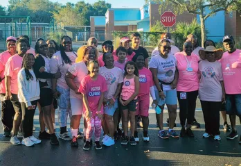 Group of people in a parking lot, wearing pink shirts at a cancer awareness event