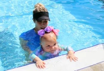 A swim instructor and baby at the edge of an outdoor pool. The FLOAT program teaches young children how to float if they fall into a body of water.  