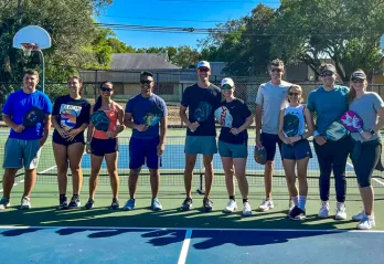 A group of adults standing side by side on an outdoor pickleball court.