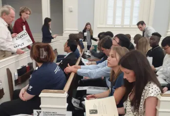 Teens in pews in a courtroom during a lecture. Foreground shows a student reading. The Youth in Government teen program attended the Florida State Assembly in February 2023. 