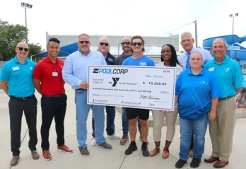 A group of adults from YMCA of the Suncoast and POOLCORP stand around presentation check on the Greater Ridgecrest YMCA pool deck.