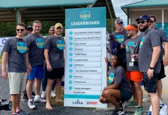 10 men and women pose by Corporate Cup Leader Board as winners for the day 