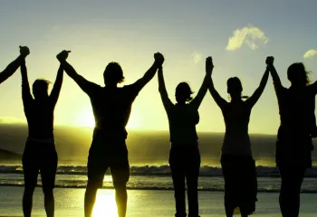 silhouette of people holding raised hands on beach at sunrise