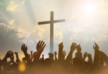 Religious cross with a sky backdrop and hands raised in prayer and worship.