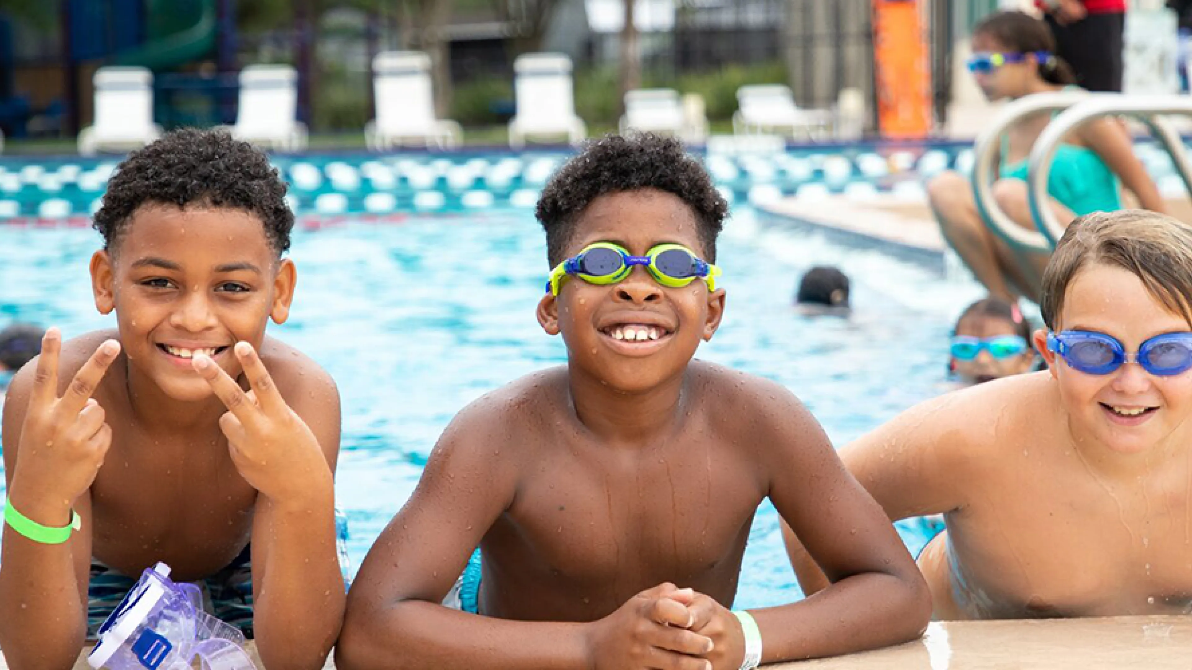 three boys smiling leaning on the pool edge
