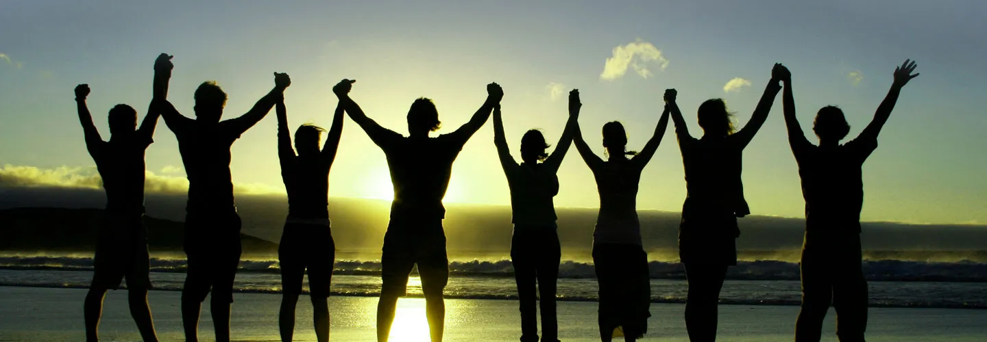 silhouette of people holding raised hands on beach at sunrise