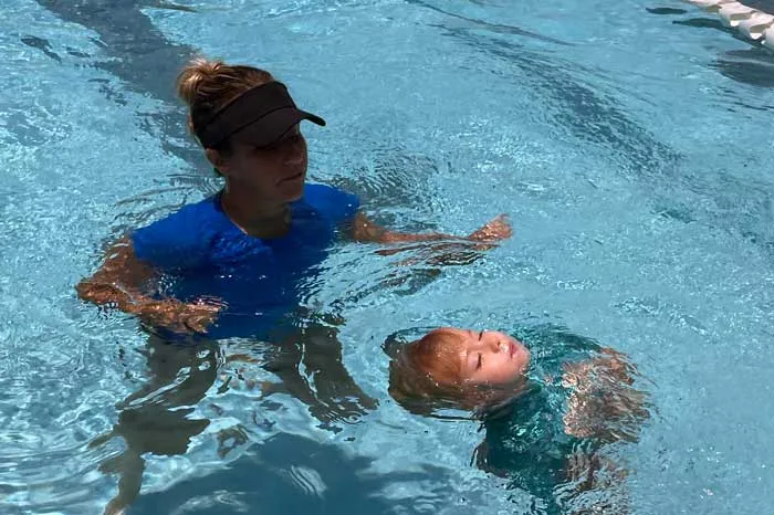 Swim instructor standing in pool inches away from toddler practice lifesaving water safety skills.