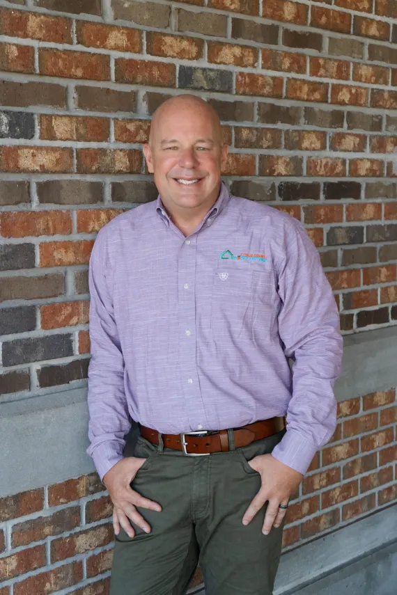 Cregg Dalton in purple button up shirt with grey pants and brown belt.