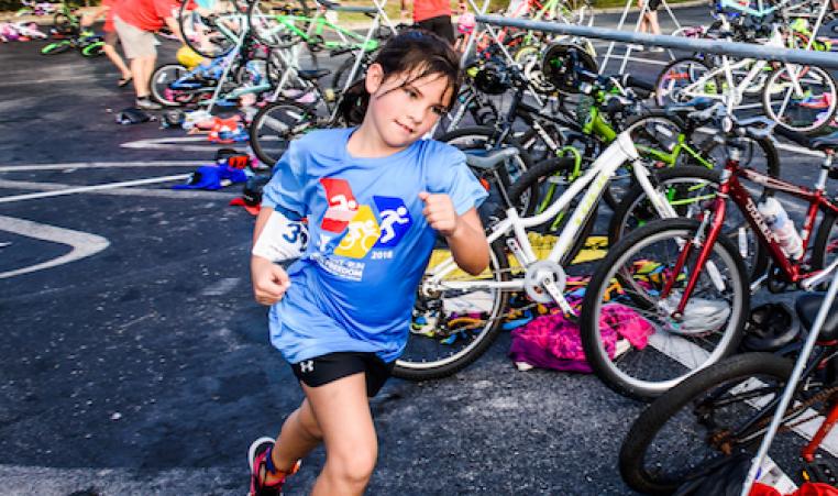 girl triathlon contestant running by bikes