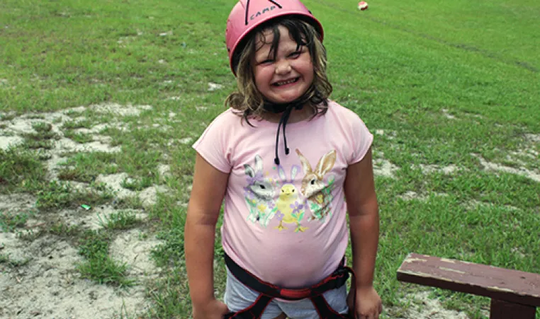 girl in a grassy field wearing a pink shirt and helmet smiling for the camera