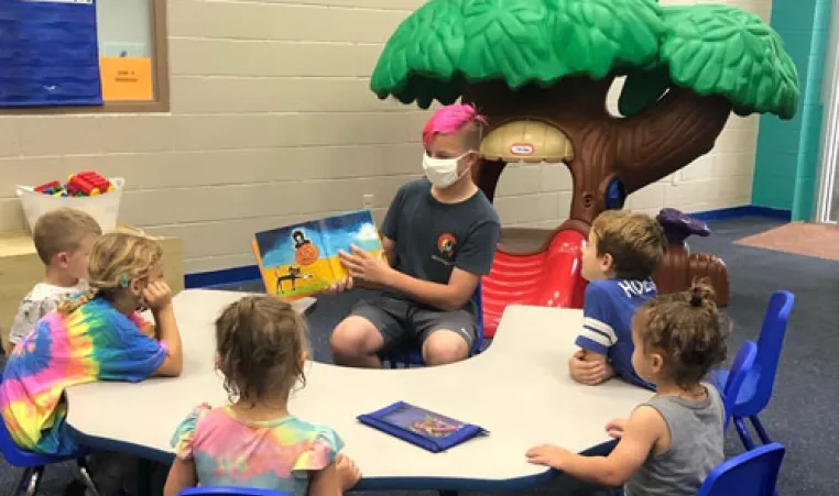 middle school student reading to group of five young children at a table in the Greater Palm Harbor Kid Zone