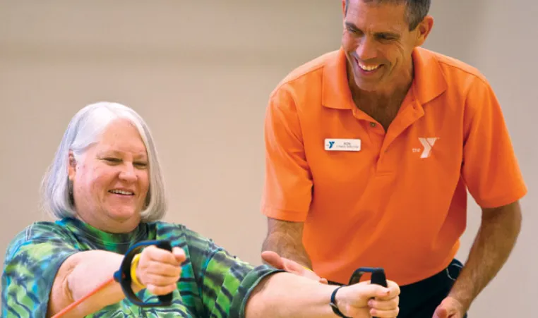 Senior using resistance bands in hands with a trainer.