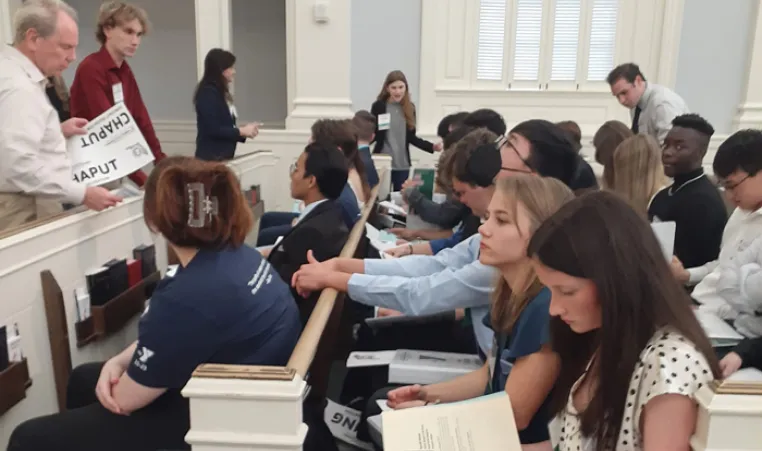 Teens in pews in a courtroom during a lecture. Foreground shows a student reading. The Youth in Government teen program attended the Florida State Assembly in February 2023.
