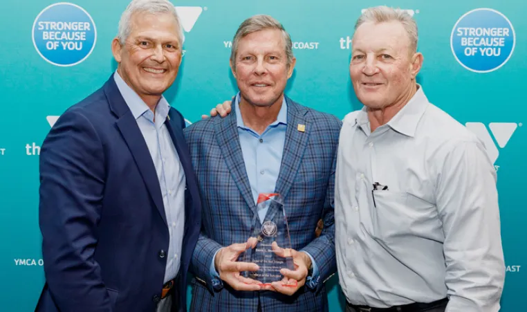 Three men on step and repeat at 2022 Annual Celebration. Man in the middle is holding a glass Order of the Red Triangle award.