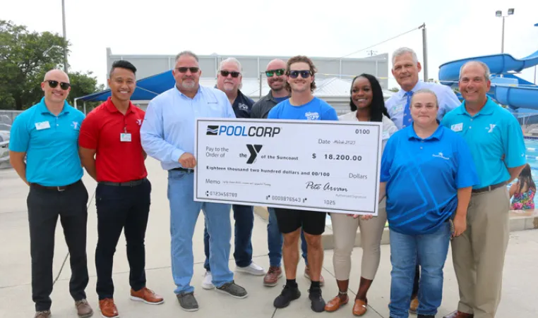 A group of adults from YMCA of the Suncoast and POOLCORP stand around presentation check on the Greater Ridgecrest YMCA pool deck.