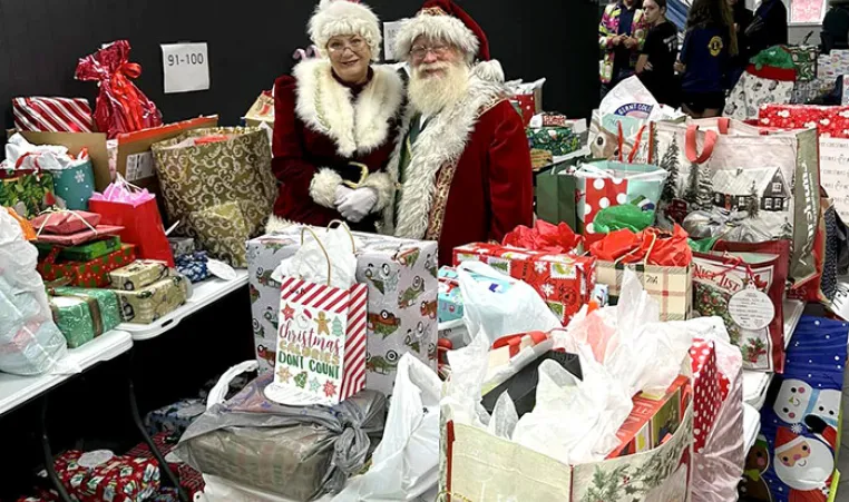 Santa and Mrs. Clause stand around many bags for Giving Tree Gifts.