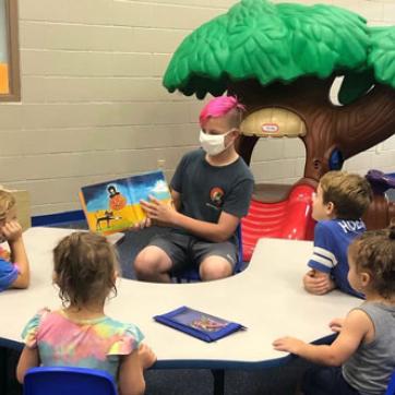 middle school student reading to group of five young children at a table in the Greater Palm Harbor Kid Zone