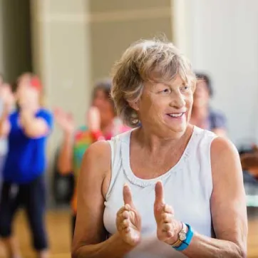 senior woman smiling and clapping in an indoor group exercise class