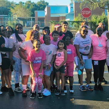 Group of people in a parking lot, wearing pink shirts at a cancer awareness event