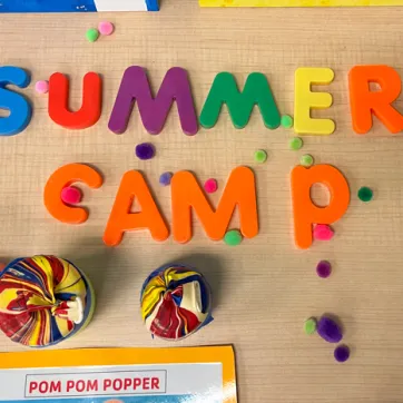 Camp craft call pom pom popper shot from above. Child play letters spell summer camp. Pom poms scattered on the table scene.