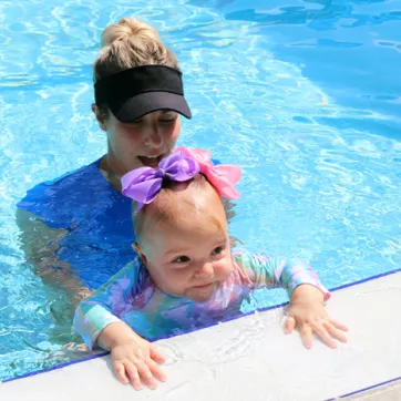 A swim instructor and baby at the edge of an outdoor pool. The FLOAT program teaches young children how to float if they fall into a body of water.  