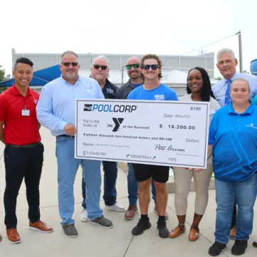 A group of adults from YMCA of the Suncoast and POOLCORP stand around presentation check on the Greater Ridgecrest YMCA pool deck.