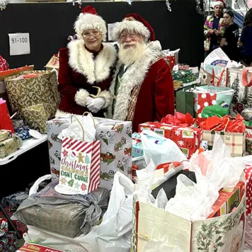 Santa and Mrs. Clause stand around many bags for Giving Tree Gifts.