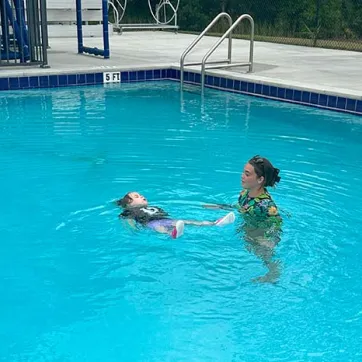 Swim Instructor teaching a young student how to float in the water.