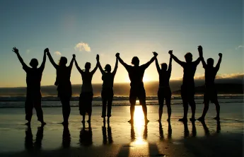 A group of people holding hands on beach as they face the sunset
