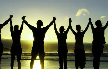 silhouette of people holding raised hands on beach at sunrise