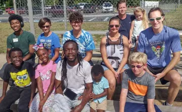 A group of dads and their kids take a break on the bleachers during family kickball.