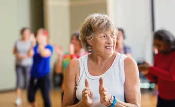 senior woman smiling and clapping in an indoor group exercise class