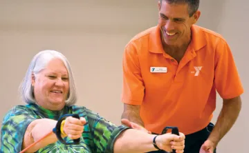 Senior using resistance bands in hands with a trainer.