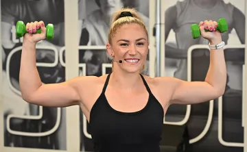 Exercise instructor smiling and flexing muscles while holding weight.s