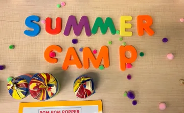Camp craft call pom pom popper shot from above. Child play letters spell summer camp. Pom poms scattered on the table scene.