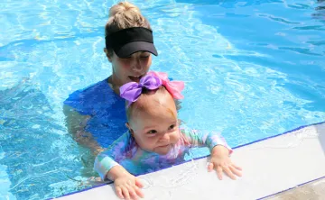 A swim instructor and baby at the edge of an outdoor pool. The FLOAT program teaches young children how to float if they fall into a body of water.  