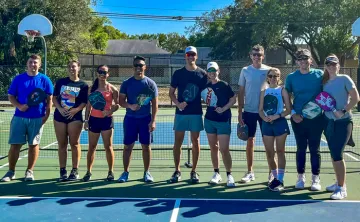 A group of adults standing side by side on an outdoor pickleball court.