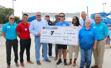 A group of adults from YMCA of the Suncoast and POOLCORP stand around presentation check on the Greater Ridgecrest YMCA pool deck.