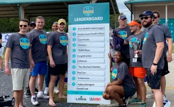 10 men and women pose by Corporate Cup Leader Board as winners for the day 