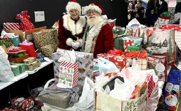 Santa and Mrs. Clause stand around many bags for Giving Tree Gifts.